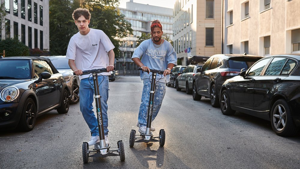 Zwei Erwachsene fahren einen E-Scooter durch die Stadt.