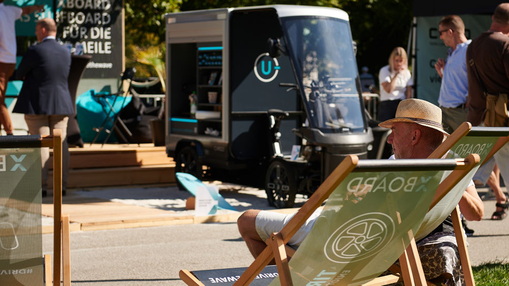 Vor dem Barista E-Lastenrad sitzt ein Mann entspannt auf einem Liegestuhl.