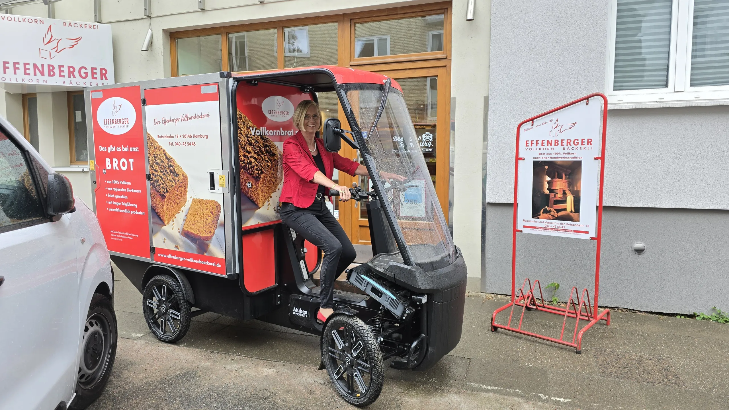 Frau auf E-Cargobike der Bäckerei Effenberger vor einer Filiale, bereit für nachhaltige Auslieferung.