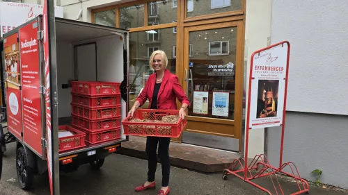Frau vor Effenberger-Filiale mit roter Backwarenkiste, belädt nachhaltiges E-Cargobike für Auslieferung.
