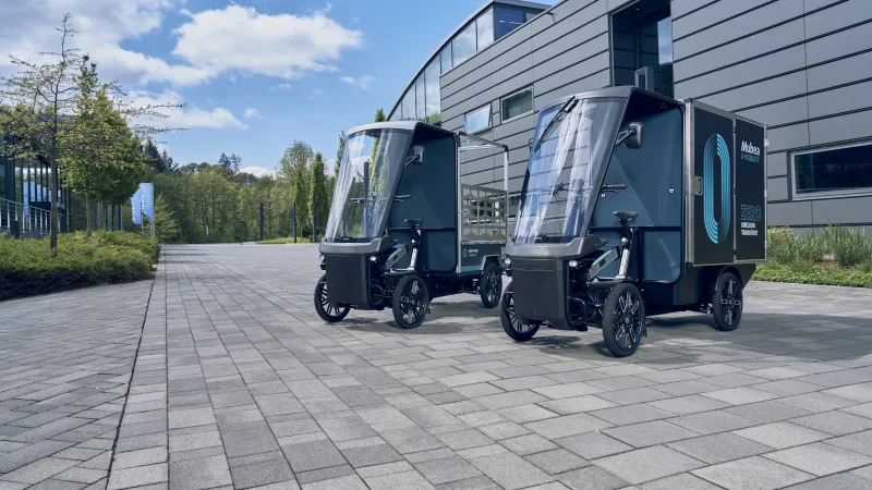 Zwei E-Cargobikes parken vor modernen Industriegebäude bei Sonnenschein.