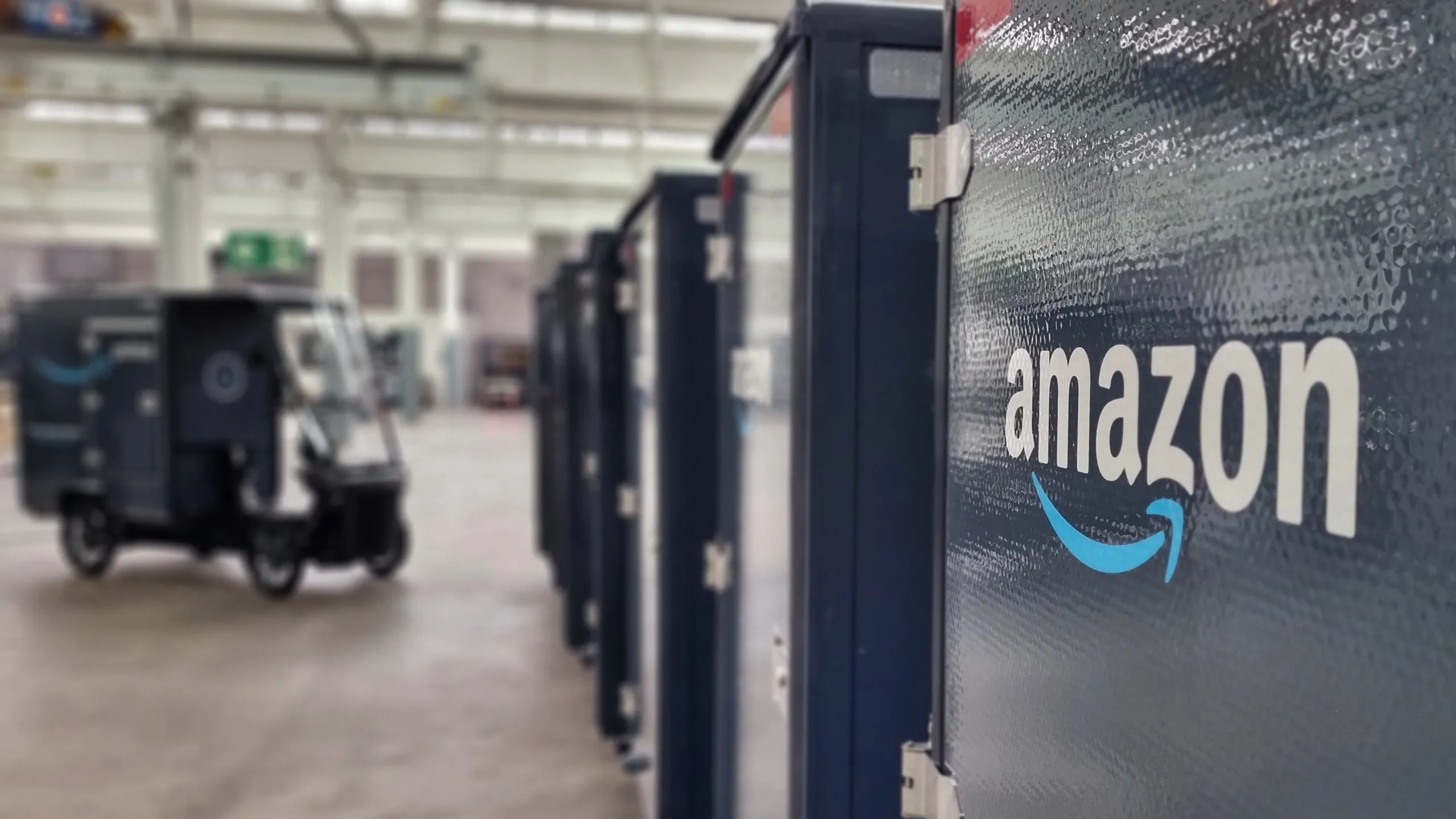 Nahaufnahme eines Amazon-Cargobikes in Lagerhalle, weitere E-Fahrzeuge im Hintergrund sichtbar.