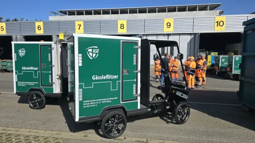 Mehrere Mitarbeiter von U-Mobility und der Abfallwirtschaft und Stadtreinigung Freiburg GmbH mit mehreren Cargo PACKs, die grün foliert sind und auf denen "Gässleflitzer" steht auf dem Gelände der ASF