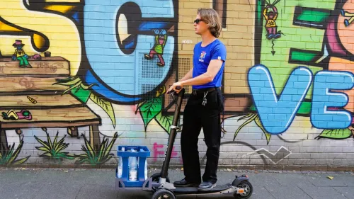 Digital X 2024: Fahrer transportiert einen Wasserkasten mit einem E-Scooter