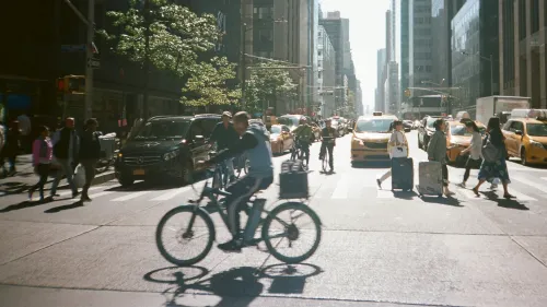 Frontal view of a street in New York, people crossing a zebra crossing, cyclists in the foreground.