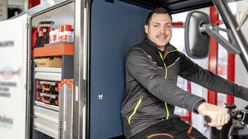 Junger Mann fährt mit einem E-Cargobike vor einem moderenem Gebäude.