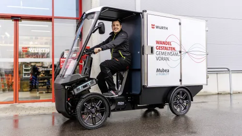 Junger Mann fährt Würth E-Cargobike vor moderner Fassade.
