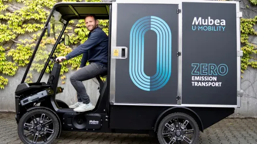 Konrad Martin fährt ein Mubea E-Cargobike mit Transportbox vor begrünter Wand