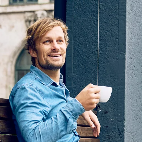 Junger Mann im Jeanshemd macht Pause und trinkt einen Kaffee.