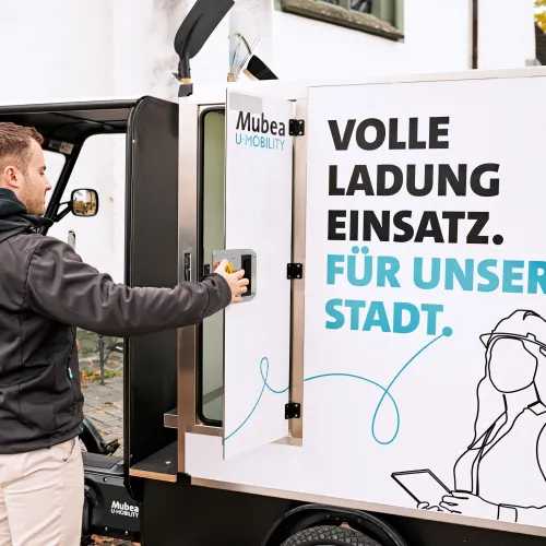 Junger Mann öffnet den Box-Aufbau eines E-Cargobikes.  
