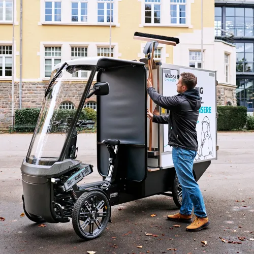 Young man removes road cleaning tools from the holder on the eCargobike.