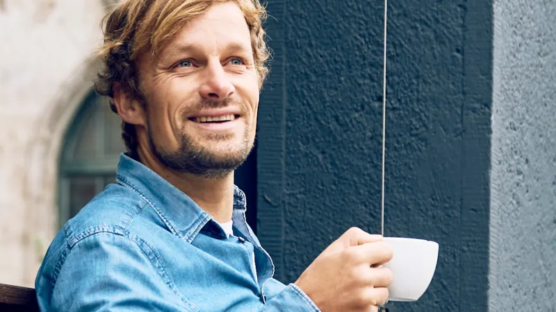 Junger Mann im Jeanshemd macht Pause und trinkt einen Kaffee.