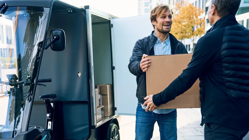 Junger Lieferant überreicht lachend ein Paket an Kunden.