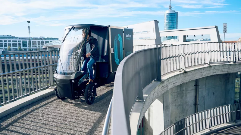 PACK auf einer Fahrradbrücke in München vor einer Skyline moderner Gebäude.