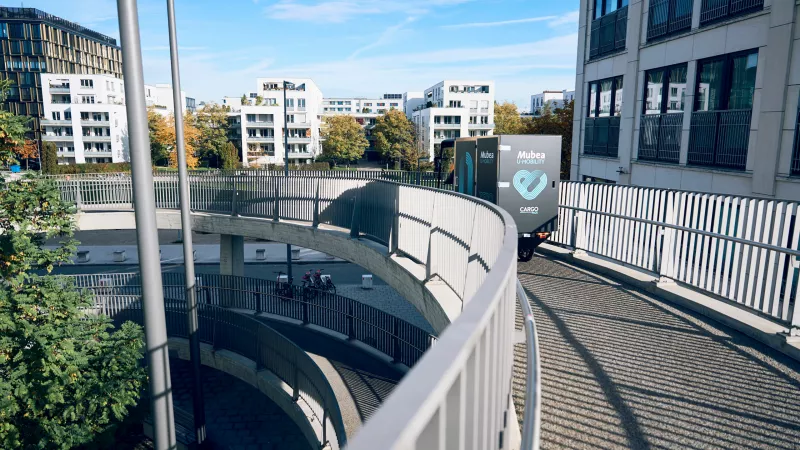 PACK von hinten auf einer Fahrradbrücke in München – im Hintergrund sind moderne Gebäude.