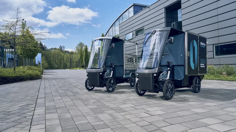 Zwei E-Cargobikes parken vor modernen Industriegebäude bei Sonnenschein.